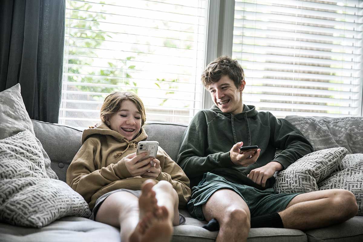 En ung tjej och en killer sitter med varsin mobil i handen i en soffa och ler mot varandra